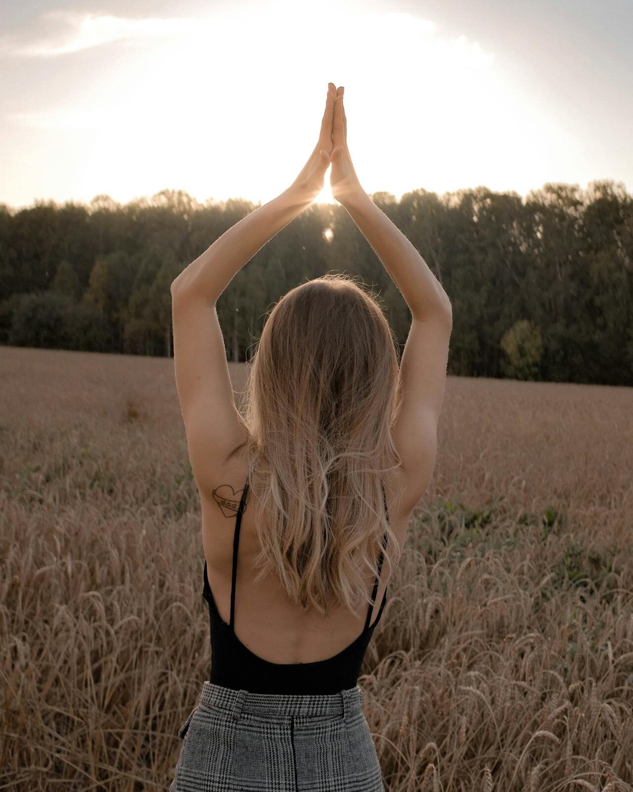 Person standing in an open field at golden hour, facing away, wind in hair