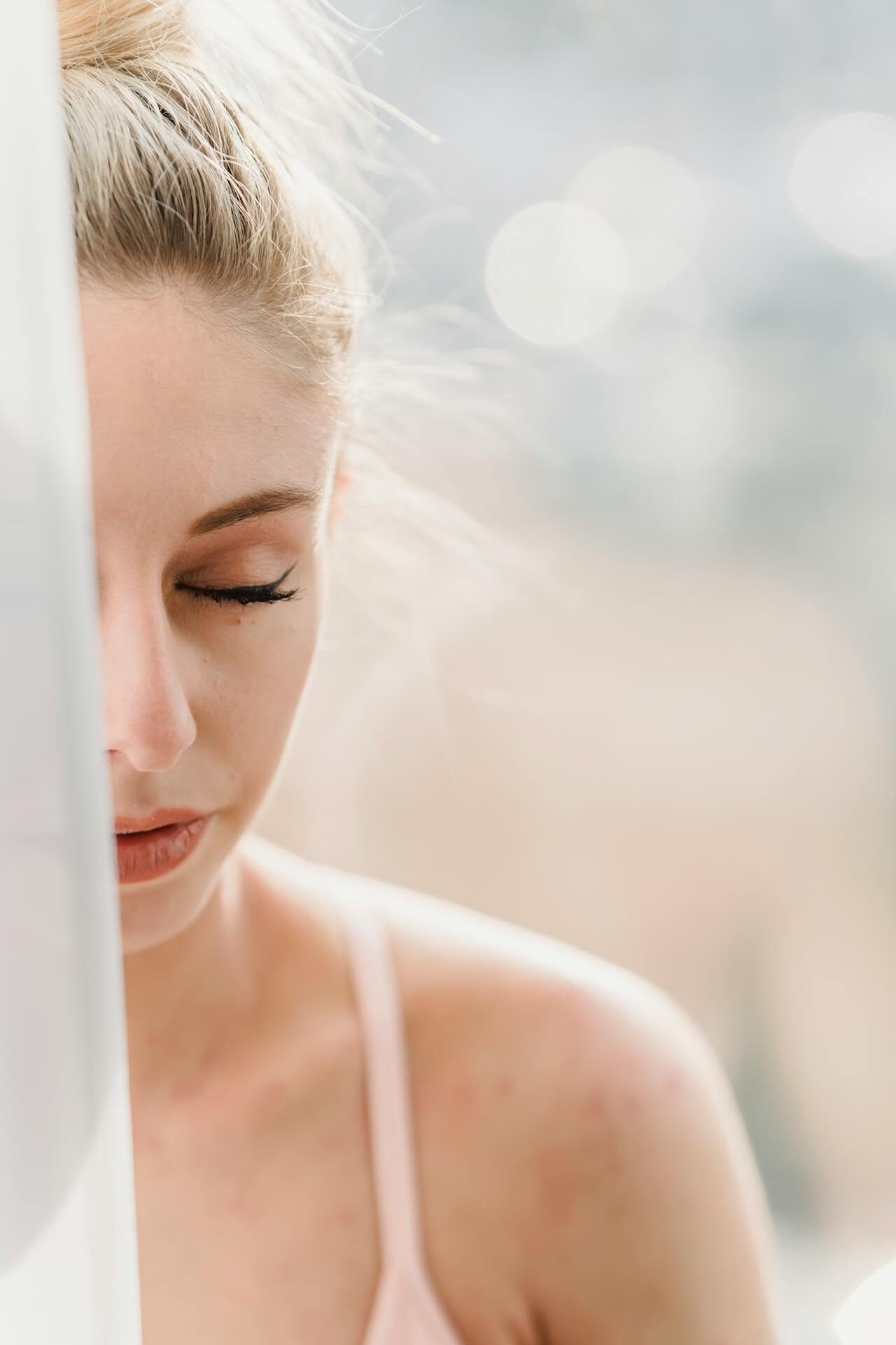 Person with closed eyes sitting near a window, soft natural light on their face