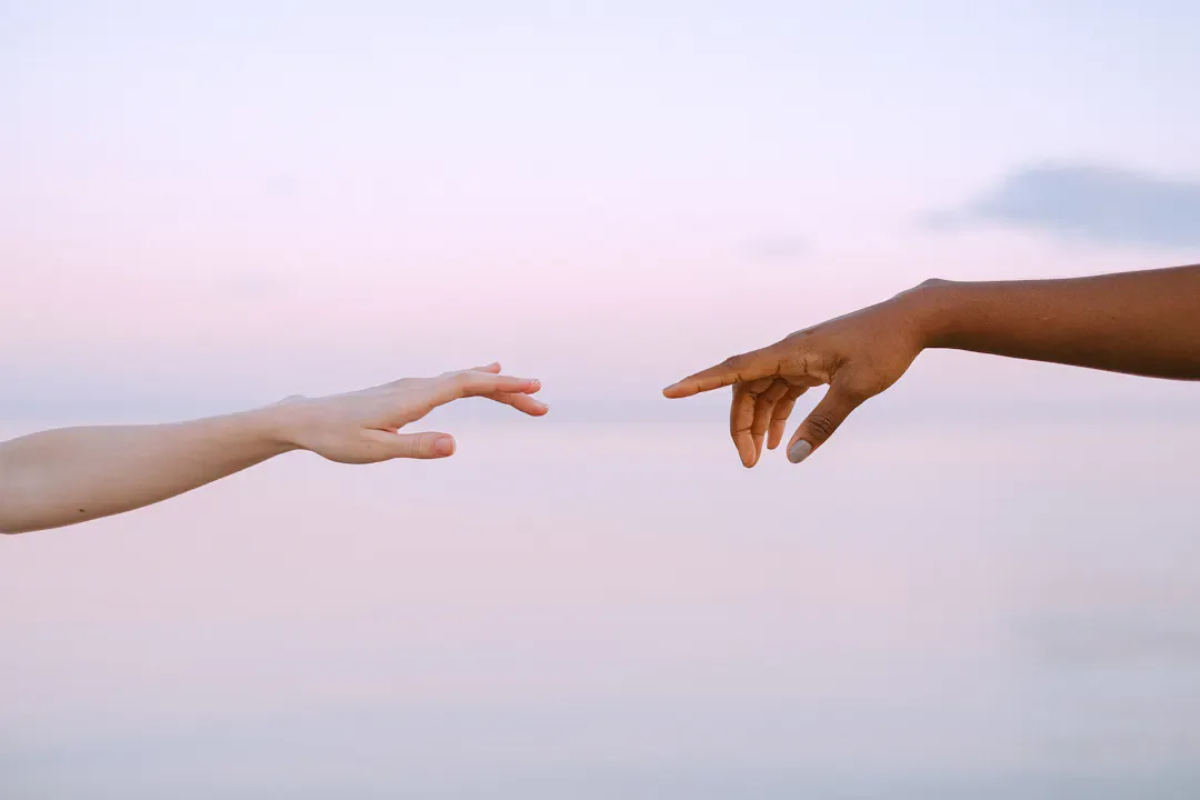 Two hands reaching towards each other in warm golden light