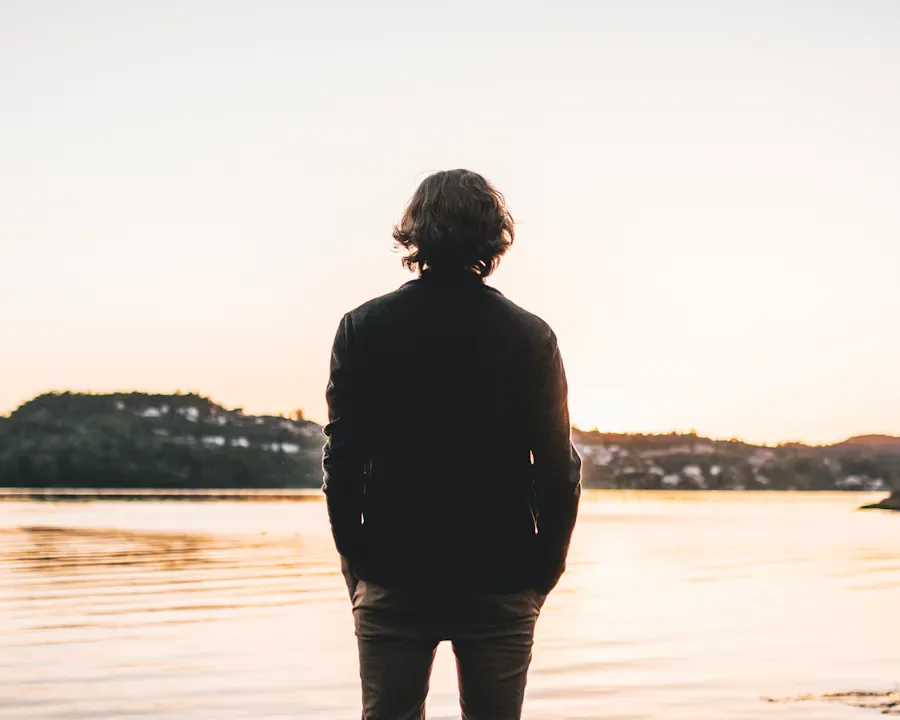 Person standing at the edge of a still lake, looking at the water