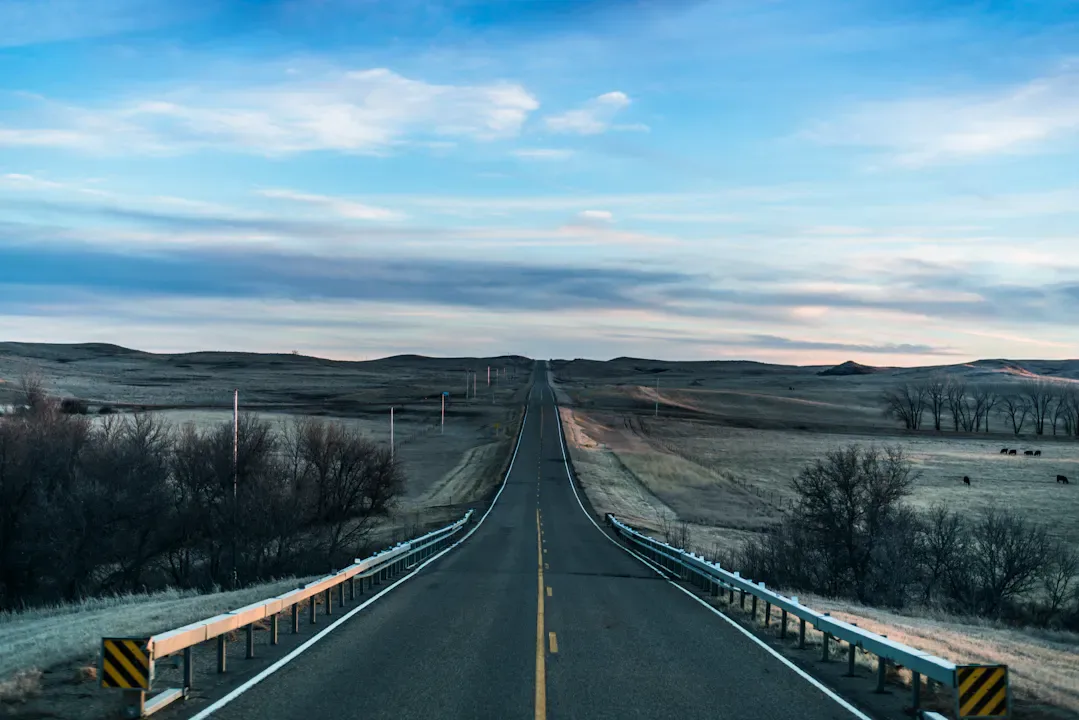 Person standing at a crossroads on a quiet country road at dawn