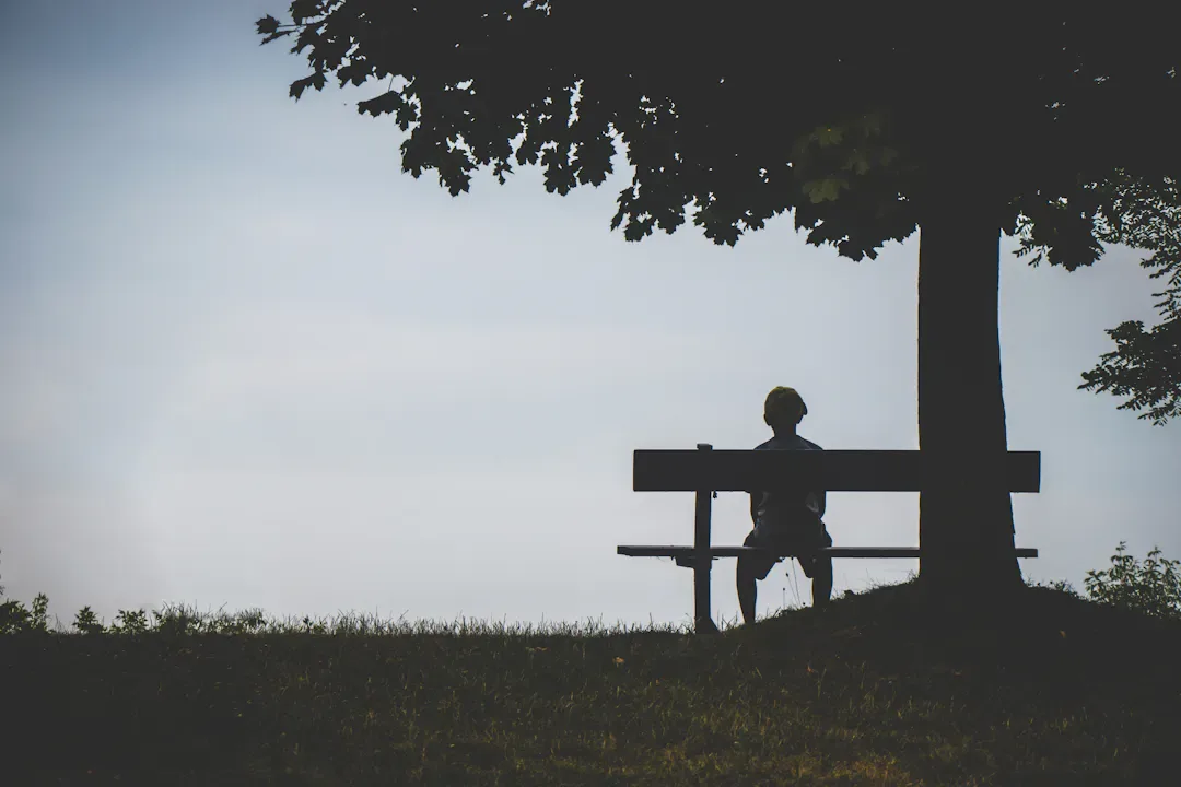 Person sitting quietly on a bench in a garden, lost in thought