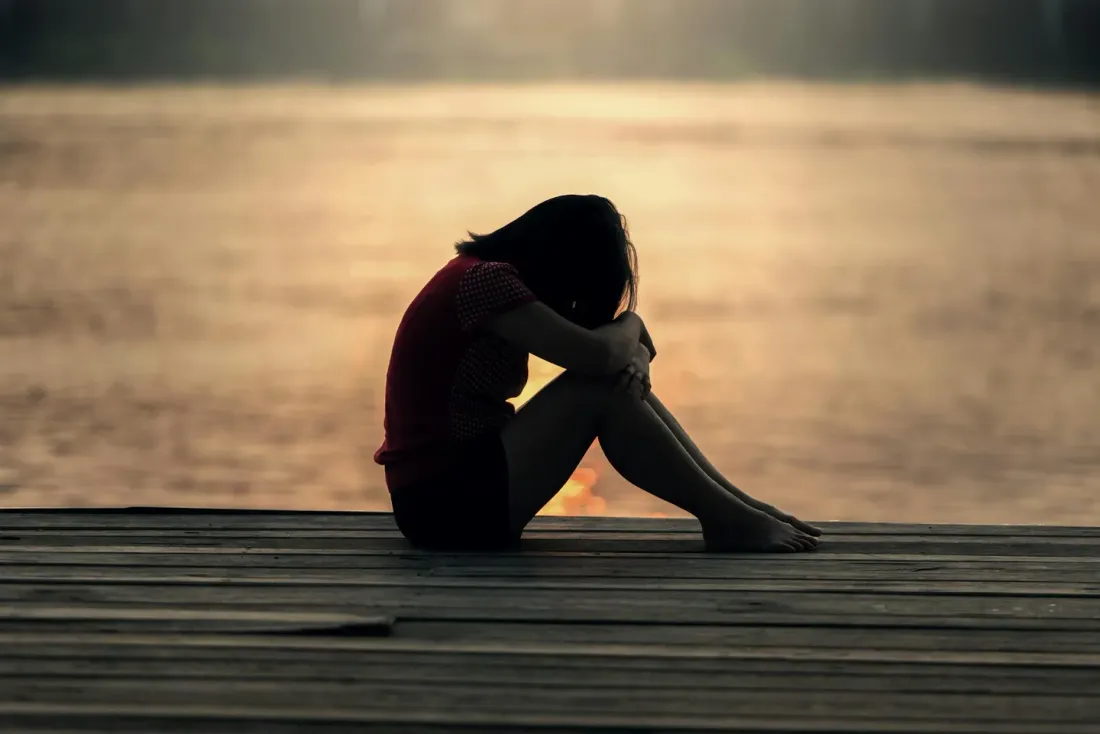 Silhouette of a person sitting on a wooden dock by the water